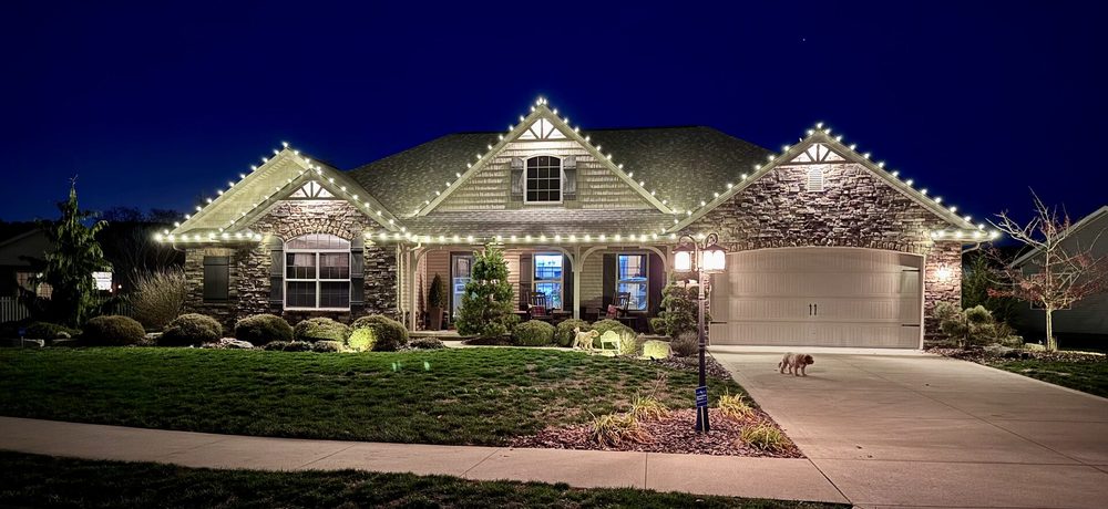 Warm white lighting on a stone and shake craftsman home and its front beds at dusk