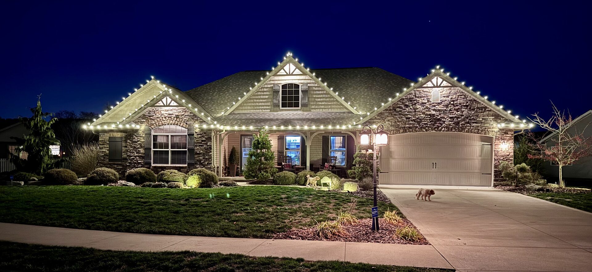 Warm white roofline lighting on a stone and shake craftsman home at dusk